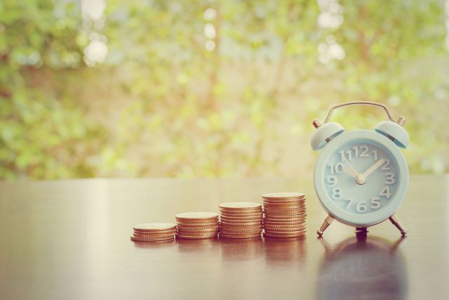 an alarm clock next to a stack of coins.